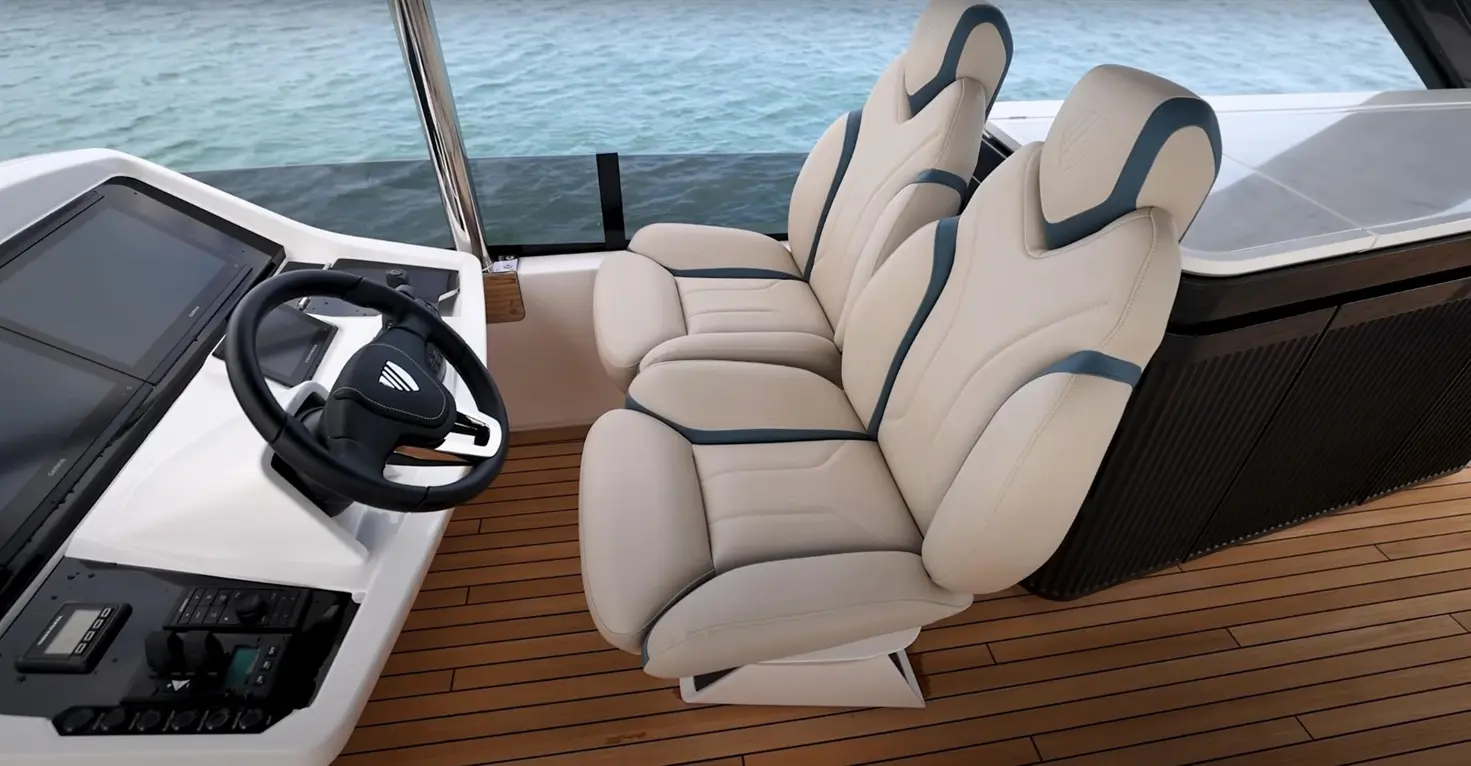 Boat interior featuring a stylish steering wheel, dual screens, and comfortable, modern captain's seats against a coastal backdrop.